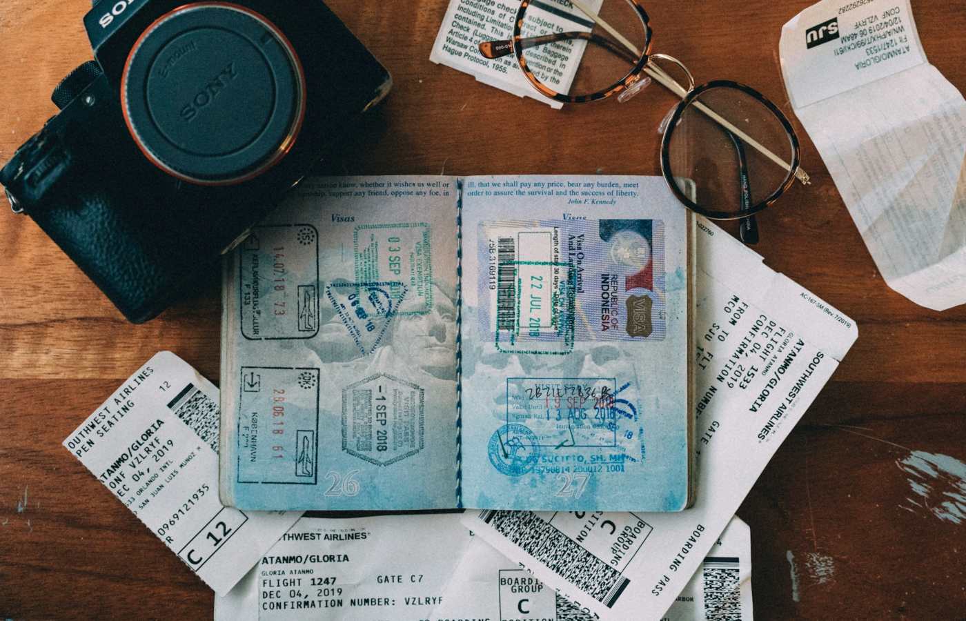 Mesa com diversos objetos, incluindo uma câmera, um óculos e um passaporte vencido